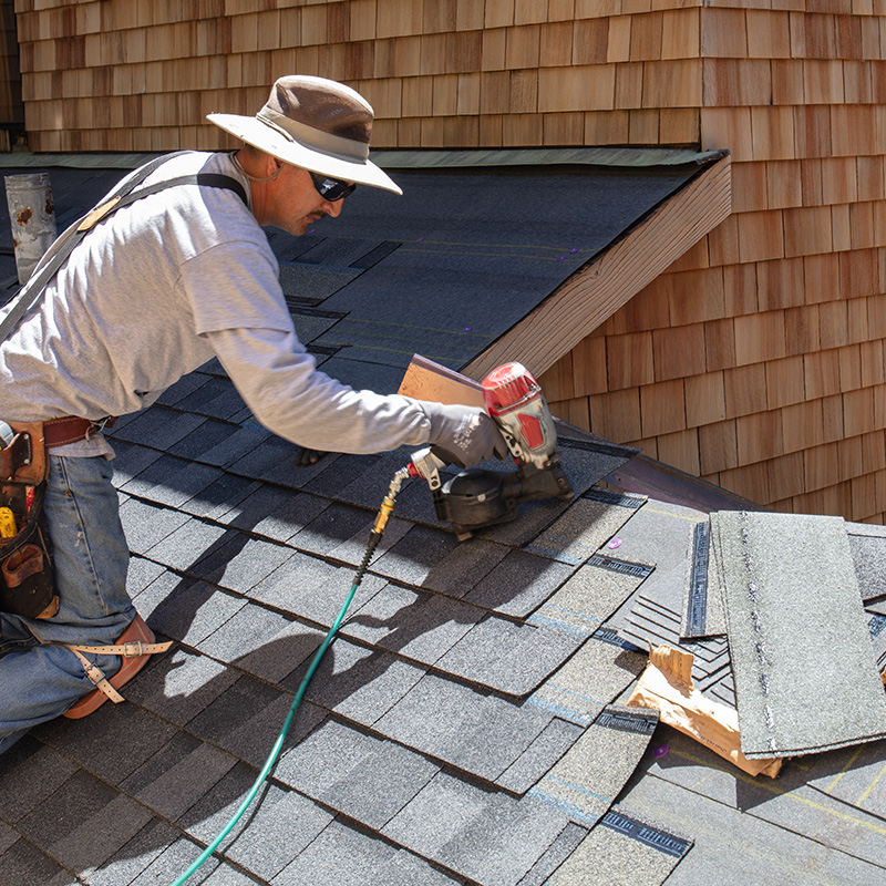 Installing new asphalt roof with nail gun and shingles